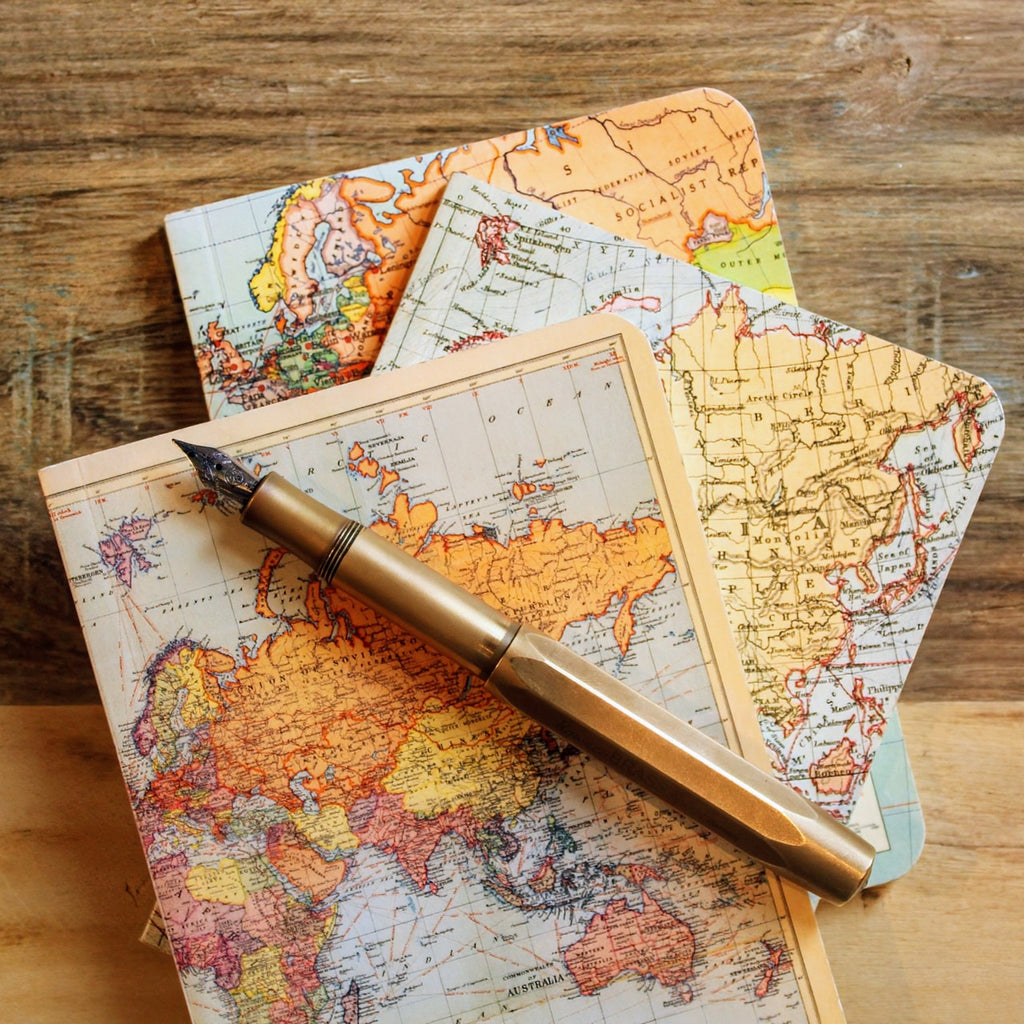 Stacked mini notebooks with vintage cartography-inspired designs, with a fountain pen resting on top.