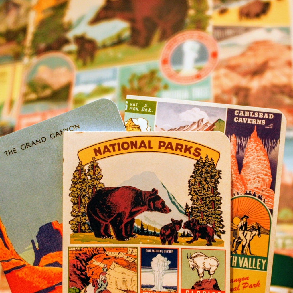 National Parks Mini Notebook Set featuring three covers with vintage-style illustrations of iconic U.S. landscapes held in front of a National Parks Poster.