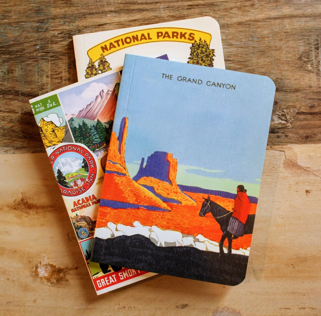 Stacked mini notebooks with retro poster-inspired covers celebrating America's national parks.