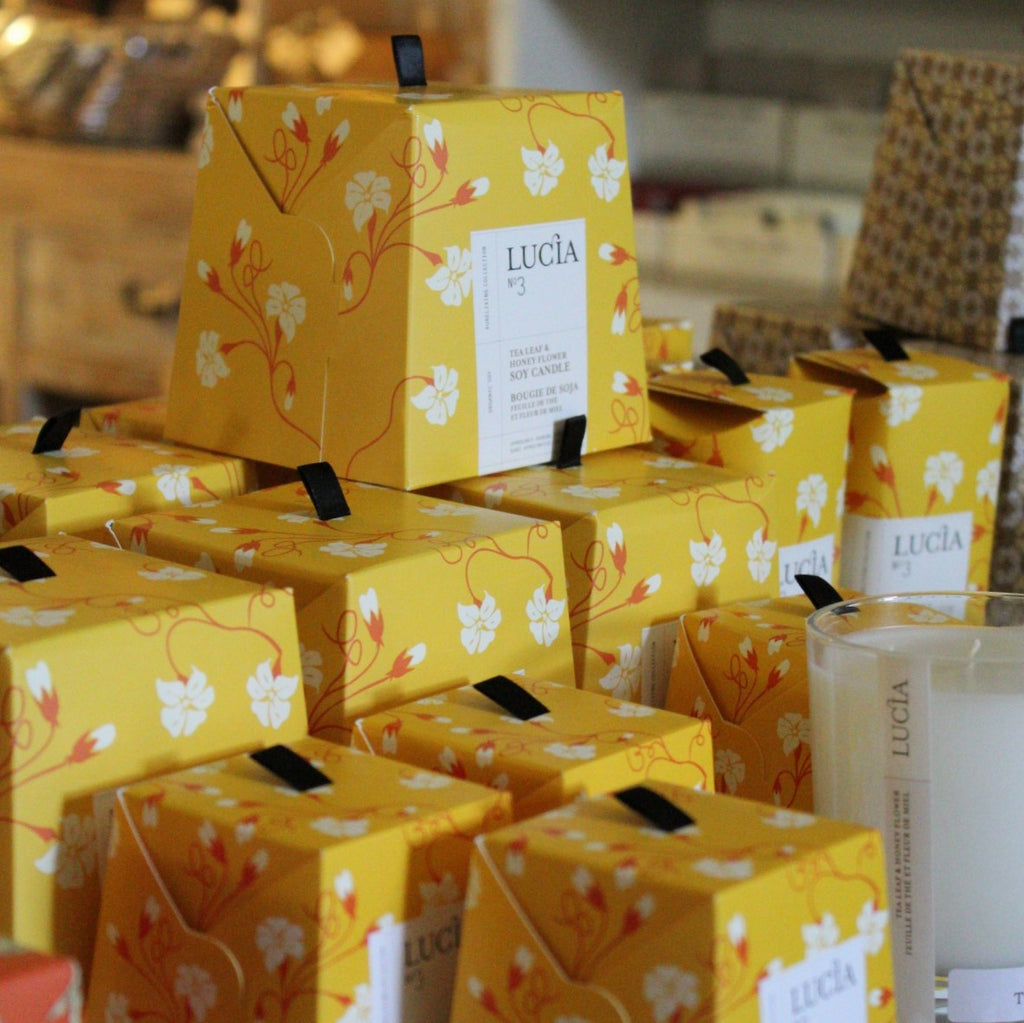 Multiple boxes of Tea Leaf & Honey Flower Soy Candles stacked on top of each other