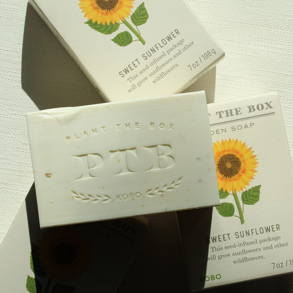 Bar of soap with 'Plant the Box' branding and sunflower design on packaging.