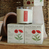 Scented soy candle with 'Plant the Box' packaging featuring red poppies on a wooden surface.