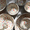 White ceramic bowls with colorful polka dots of different sizes scattered with shadows. 
