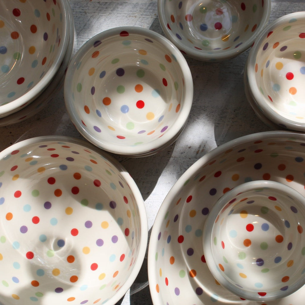 White ceramic bowls with colorful polka dots of different sizes scattered with shadows. 