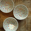 White ceramic bowls with colorful polka dots on a wooden surface.