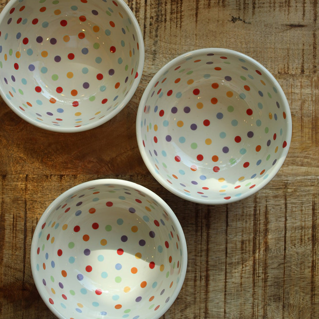White ceramic bowls with colorful polka dots on a wooden surface.