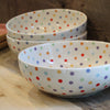 White ceramic serving bowls with colorful polka dots on a wooden surface.
