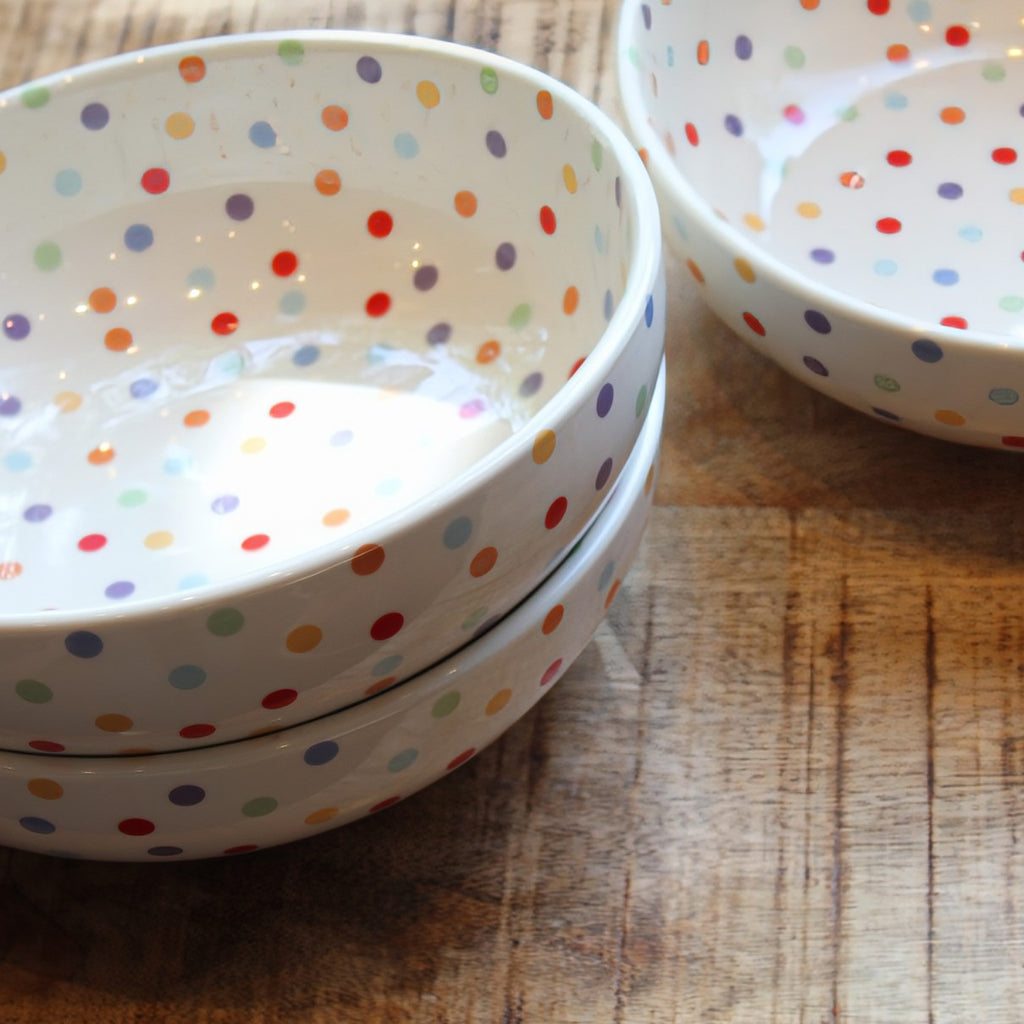 White ceramic serving bowls with colorful polka dots on a wooden surface.