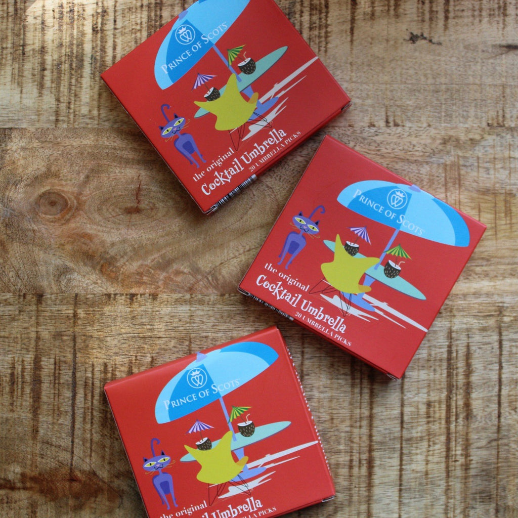 Three Original Cocktail Umbrella boxes flat on a wooden surface