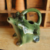 Green stonewate watering pitcher in the shape of a frog with an open mouth on a wooden surface