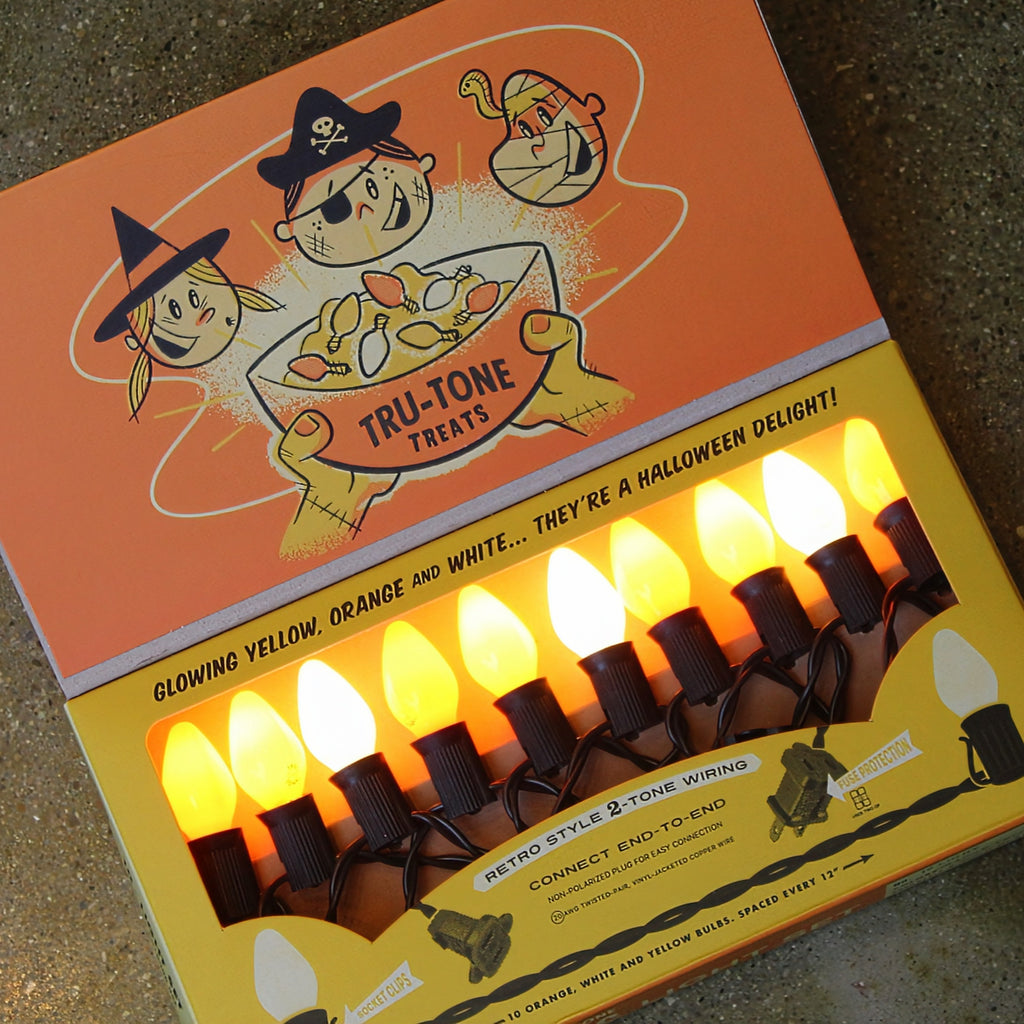 A box of Tru-Tone Halloween-style lights with illustrated pirate and witch graphics on the lid, shown open to reveal multiple yellow orange and white  glowing bulbs in a windowed lower section.