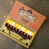 A package of Halloween 'Tru-Tone Treats' string lights, shown open on a concrete floor. The box is orange and yellow with cartoon illustrations of a witch, a ghost, and a pumpkin.