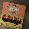 A box of Tru-Tone Halloween string lights with retro-style bulbs in orange, yellow, white, on a black cord, shown in its illustrated packaging on a dark textured surface.