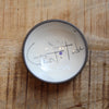 A small handmade ceramic bowl with a dark exterior and a white interior, featuring the handwritten word 'Gratitude' in black with a small colorful dot, placed on a wooden surface.