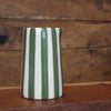 A glossy ceramic pitcher with vertical green and white stripes, standing on a wooden surface against a rustic wooden plank background.