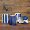 Four white ceramic mugs with blue painted stripes, arranged on a wooden surface against a rustic wooden plank background.