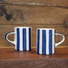 Two white ceramic mugs with vertical navy blue stripes, displayed side-by-side on a wooden surface against a rustic wooden plank background.