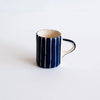A small ceramic mug with a navy blue exterior featuring vertical hand-painted stripes, with a white interior and handle, set against a plain white background.