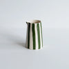A glossy ceramic pitcher with vertical green and off-white stripes, set against a plain light gray background.
