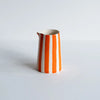 Ceramic pitcher with orange and white stripes on a light gray background