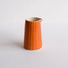 An orange ceramic pitcher with thin vertical white stripes and a small pouring spout, set against a plain light gray background.